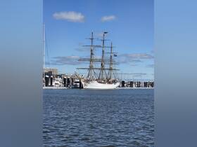 A majestic sailing ship is seen cruising in the harbor, showcasing its impressive masts and rigging against a clear blue sky.