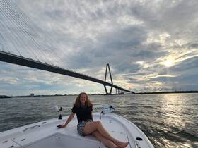 A woman relaxes on the bow of a boat with a stunning view of a bridge at sunset, capturing the essence of a perfect day on the water.