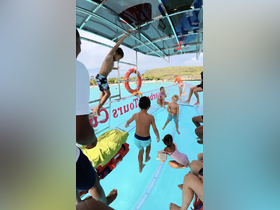 A lively scene of children enjoying a fun day on the water, jumping off a boat and swimming in crystal-clear waters — perfect for family adventures.