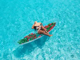 A woman relaxes in a clear boat adorned with flowers, floating in stunning turquoise waters — a perfect scene for tropical getaways and relaxation.