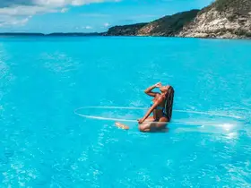 A woman enjoys a refreshing drink while paddleboarding in stunning aquamarine waters — a perfect moment of relaxation and fun in the sun.