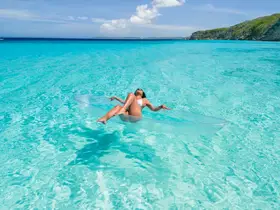 A woman relaxes on a clear inflatable float in the stunning turquoise waters, showcasing the perfect beach day experience.