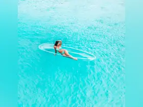 A woman relaxes on a clear floating mat in stunning aquamarine waters, embodying the ultimate beach day experience.