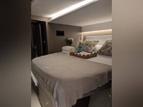 A cozy and elegantly designed cabin interior featuring a neatly made bed with decorative pillows and a refreshing drink, perfect for relaxing on a yacht.