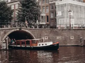 A charming scene in Amsterdam featuring a boat navigating the canal, with people enjoying the picturesque surroundings — a perfect representation of the city's vibrant atmosphere.