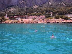 Swimmers enjoy the crystal-clear waters near a picturesque beach, surrounded by stunning cliffs and vibrant beach umbrellas — a perfect summer getaway.