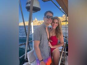 A happy couple poses on a boat with a stunning backdrop of Malta's coastline, perfect for romantic getaways and memorable adventures on the water.