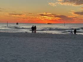 A couple enjoys a romantic sunset on the beach, with a boat in the distance, creating a picturesque scene perfect for memorable moments.