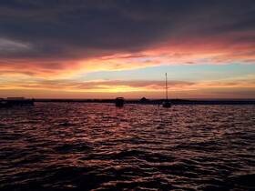 A serene sunset view over the water featuring boats silhouetted against a vibrant sky, perfect for capturing the beauty of evening cruises.