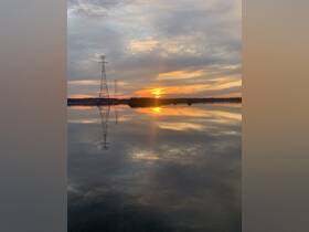 A serene sunset reflection over calm waters, with power lines silhouetted against the colorful sky.