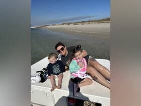 A joyful family enjoys a sunny day on a boat, with kids playing and the beach in the background — perfect for memorable family outings.