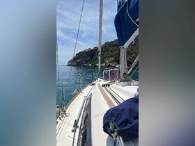 A serene view from the front of a sailboat, showcasing the vessel's sleek design against a backdrop of rocky cliffs and calm waters.