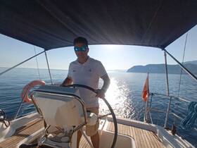 A sailor navigates the helm of a yacht, showcasing the serene waters and distant coastline — perfect for a day of sailing adventures.