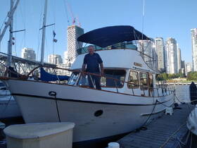 A man stands proudly on the deck of a boat named 'Resilient' at the dock, with a stunning city skyline in the background — perfect for urban boating adventures.