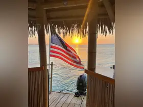 A stunning sunset view from a dock with an American flag waving, capturing the serene beauty of the water — perfect for peaceful evenings by the shore.