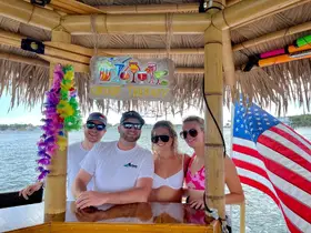 A cheerful group enjoys drinks at a tiki bar on the water, perfect for a fun day of relaxation and celebration with friends.