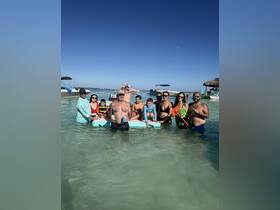 A lively family gathers in shallow waters, enjoying a day of fun and snorkeling, with boats in the background — perfect for memorable group outings on the water.