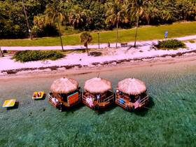 A vibrant scene featuring floating tiki huts at a beach, with guests enjoying the sun and water activities — perfect for a fun day out on the water.