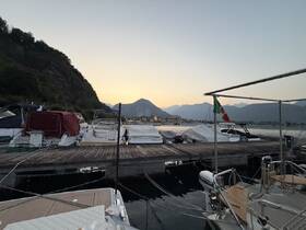 A serene view of various boats docked at sunset, with a picturesque backdrop of mountains and a charming waterfront town.