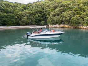 A group enjoys a relaxing day on a Marinello boat, with one person swimming nearby in the serene waters, surrounded by lush greenery and a picturesque coastline.