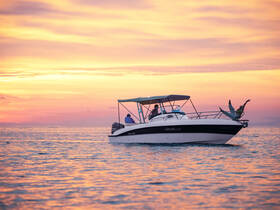 A vibrant sunset scene captures guests enjoying their time on a boat, with one person joyfully jumping into the ocean — a perfect moment of fun and adventure on the water.