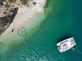 Aerial view of a group enjoying a beach day, swimming in a heart formation while a catamaran is anchored nearby — perfect for fun-filled water activities.