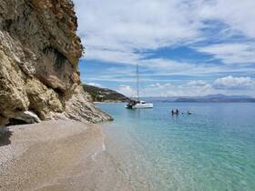 A picturesque scene featuring a catamaran anchored near a sandy beach, with people enjoying the clear waters — perfect for a relaxing day of swimming and sunbathing.