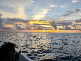 A stunning sunset over the ocean, with a silhouette of a person enjoying the view from a boat — a perfect moment for relaxation and reflection on the water.