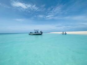 A group enjoys a relaxing day at a sandbar, with a boat anchored nearby and clear turquoise waters inviting for swimming and fun.