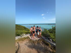 A joyful family poses for a photo at a scenic viewpoint overlooking turquoise waters, capturing a memorable moment during their beach adventure.