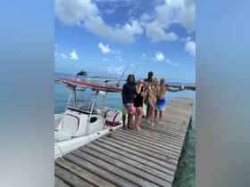 A cheerful group poses on the dock next to their fishing boat, celebrating a day on the water with drinks and smiles under a beautiful sky.