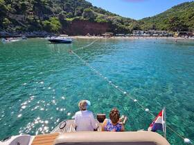 A couple enjoys a serene moment on their boat, overlooking a beautiful beach and clear turquoise waters — perfect for a relaxing day on the water.