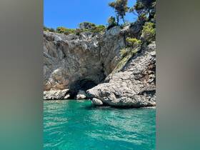 A stunning view of a rocky coastline with a cave entrance, surrounded by crystal-clear turquoise waters — a perfect destination for exploring by boat.