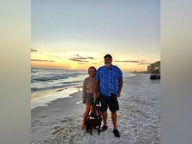 A couple enjoys a beautiful sunset on the beach with their dog, capturing a perfect moment of relaxation and joy by the ocean.
