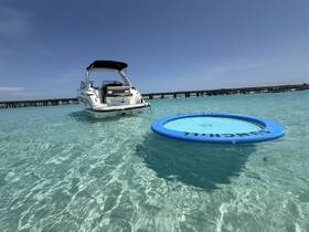 A sleek boat anchored in crystal-clear waters, featuring a floating mat nearby, perfect for fun and relaxation on a sunny day.