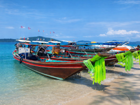 A vibrant scene of traditional longtail boats docked on a sandy beach, showcasing the beauty of coastal Thailand with clear blue waters and a picturesque backdrop.
