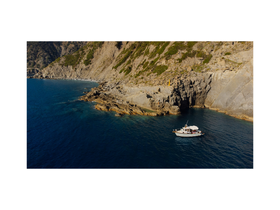 Aerial view of a boat anchored near rocky cliffs, showcasing the serene coastal landscape and clear blue waters.