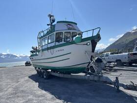 A side view of a fishing boat docked on a trailer, showcasing its structure against a scenic backdrop of mountains and water.