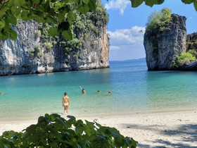 A picturesque beach scene with people enjoying the turquoise waters, surrounded by stunning rock formations — perfect for island adventures and relaxation.