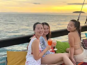 Three friends enjoy cocktails while watching a stunning sunset on a boat, capturing the essence of a perfect evening celebration on the water.