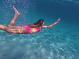 A girl swims gracefully underwater in crystal-clear waters, showcasing the beauty of snorkeling adventures in tropical destinations.