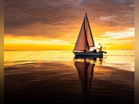 A stunning sailboat glides across calm waters at sunset, reflecting vibrant hues of orange and yellow — a perfect scene for sailing enthusiasts and sunset lovers.