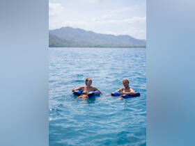 A couple enjoys a relaxing day floating in the water with drinks in hand, surrounded by stunning scenery — perfect for a fun beach getaway.