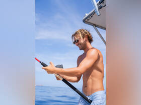 A man enjoys fishing on a sunny day at sea, showcasing the thrill of on-water activities. Perfect for adventure seekers and fishing enthusiasts.