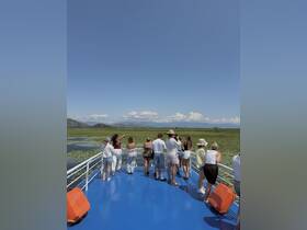 A lively group enjoys the scenic views from the deck of a boat, surrounded by lush greenery and mountains — perfect for nature exploration and sightseeing adventures.