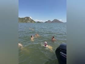 A lively group enjoys a refreshing swim in a scenic lake, surrounded by stunning hills — perfect for a fun day out on the water.