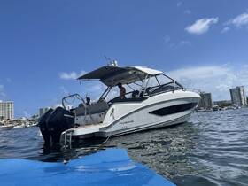 A sleek speedboat, the Flyer 32, is docked with two people visible on board, showcasing a perfect day on the water against a backdrop of clear blue skies and city buildings.