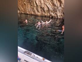 A lively group enjoys swimming in crystal-clear waters near a rocky cave, capturing the essence of adventure and fun on the water.