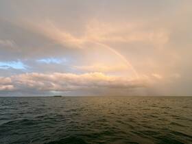 A stunning view of a rainbow arching over the ocean, framed by dramatic clouds — a picturesque moment capturing the beauty of nature at sea.