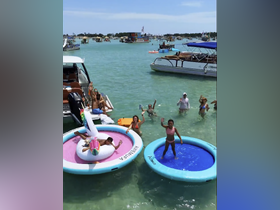 A lively group enjoys a fun day on the water with floating mats and swimming, showcasing the perfect summer party atmosphere.